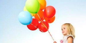Adorable young girl holds tightly to a large bunch of helium filled balloons