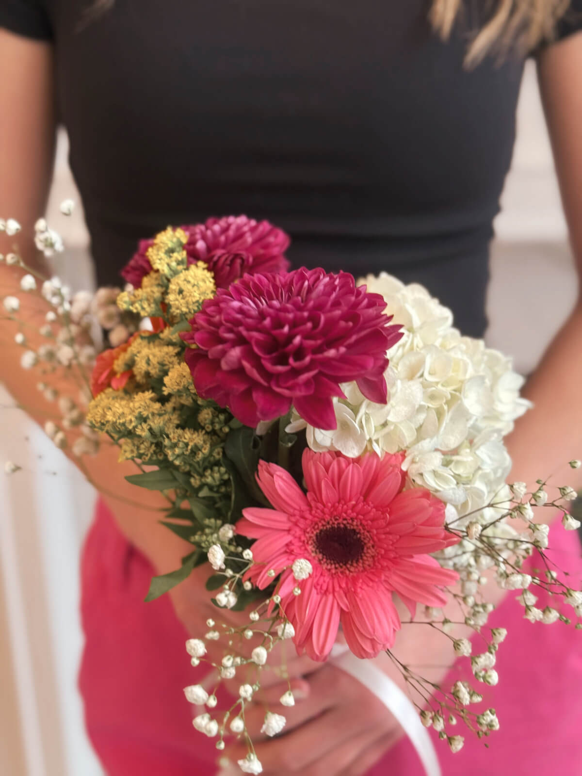 Woman holding a bright DIY flower bouquet with pink gerbera daisies, hydrangeas, chrysanthemums, and baby’s breath