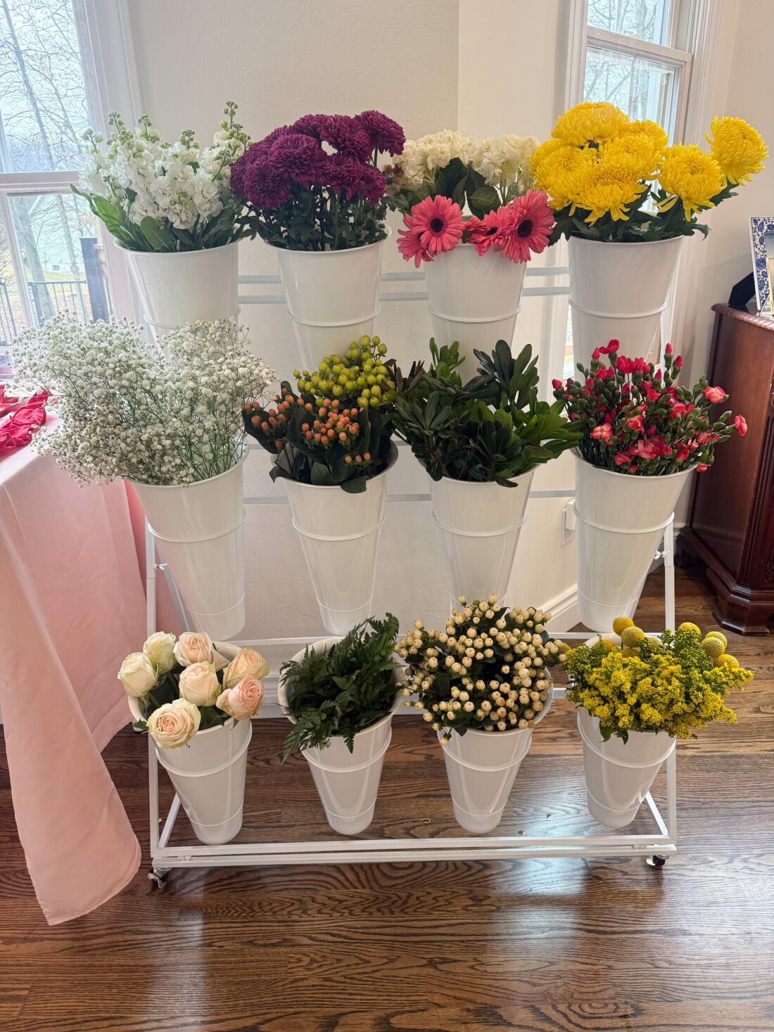 Flower bar party setup for a party with white buckets holding fresh flowers and greenery, including roses, baby’s breath, and chrysanthemums.